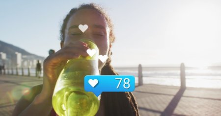 Image of heart icon with numbers over biracial female athlete drinking water against sea. Digital...