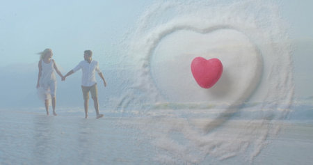 Image of hearts over happy diverse couple holding hands on beach by sea. Love, relationship, home and lifestyle concept digitally generated image.の写真素材