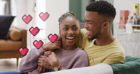 Image of hearts over happy diverse couple on sofa at home. Love, relationship, home and lifestyle...