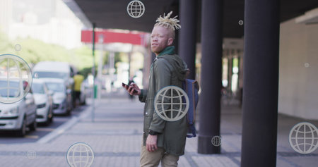 Image of globe icons over albino african american man walking while looking backward on street. Digital composite, multiple exposure, globalization, business, abstract and technology concept.の写真素材