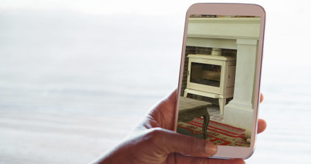 Image of person using smartphone with house sitting room fireplace interiors displayed on screen....