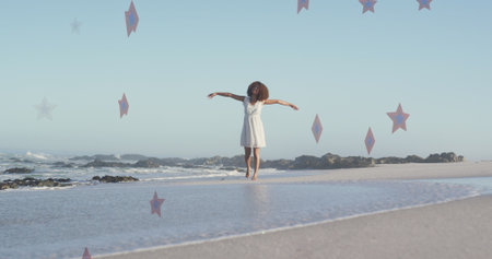 Image of stars over african american woman raising hands at beach. patriotism and celebration concept digitally generated image.の写真素材
