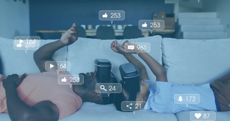 Image of social media icons and numbers over african american father and son using vr headset....