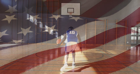 Middle-aged African American man in jersey dribbles basketball. He has short black hair, playing in gym overlaid with American flagの写真素材