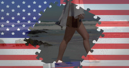 Image of flag of usa with puzzle pieces over caucasian woman walking on beach. Patriotism and celebration concept digitally generated image.の写真素材