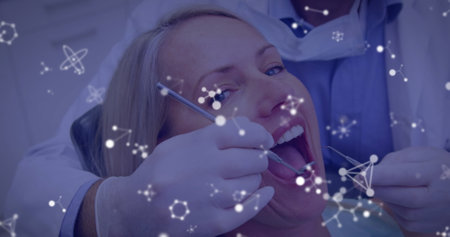 Image of molecules flowing over male dentist with face mask treating female patient in dentist chair. Medical dental treatment Covid 19 coronavirus protection concept digital composite.の写真素材