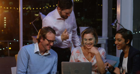 Caucasian male and female chefs, biracial female assistant view laptop. They are indoors at night,...