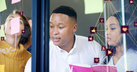 Image of two globes of digital icons over diverse office colleagues discussing over memo notes. Global networking and business technology conceptの写真素材