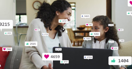 Image of icons with growing number over biracial woman and her daughter using laptop. Global social media and digital interface concept digitally generated image.の写真素材
