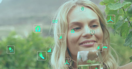 Image of ecology icons over caucasian woman with glass of wine. Global ecology and digital interface concept digitally generated image.の写真素材