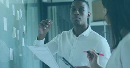 Black man and white woman discuss graphs. He has short black hair, wearing white shirt; she has long...