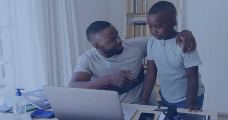 African American father pointing at laptop screen, son watching closely. Both wearing casual clothes, surrounded by books and blue backgroundの写真素材
