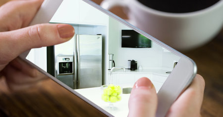 Image of person using smartphone with house kitchen interiors displayed on screen. Online shopping house decorating concept digital composite.の写真素材