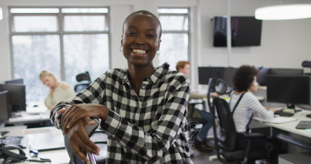 African American female partner leaning on chair, smiling in office. She has short black hair, clear skin, and is wearing a checkered shirtの写真素材