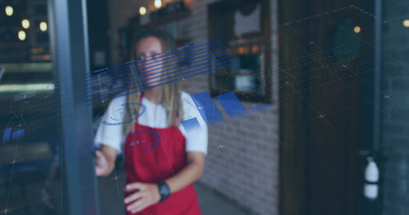 Biracial young professional wearing red apron, cleaning glass door. Sporting short black hair, using...