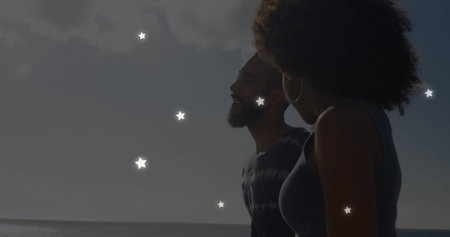 Image of stars over diverse couple at beach. Free time and digital interface concept digitally generated image.の写真素材