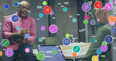 Image of network of digital icons over diverse man and woman discussing at office. Global networking...