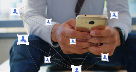 Image of network of profile icons over mid section of caucasian man using smartphone at office. Social media networking and business technology conceptの写真素材