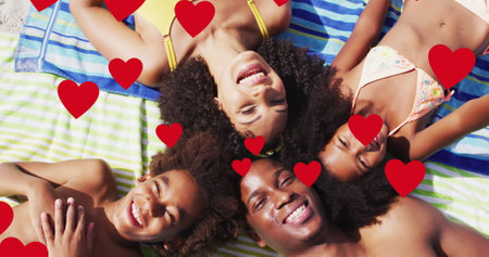 Image of red hearts over smiling african american family on holiday lying on beach towels. family, holidays, love and togetherness concept digitally generated image.の写真素材