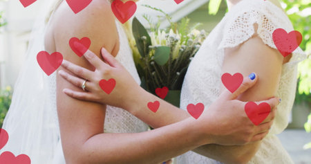 Image of hearts over diverse female married couple embracing. Pride, lifestyle and celebration concept digitally generated image.の写真素材