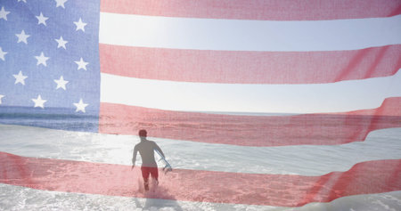 Image of american flag over biracial man with surfboard walking into sunny sea. America, summer,...