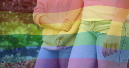 Image of rainbow flag over diverse female couple holding hands. Pride, lifestyle and celebration concept digitally generated image.の写真素材