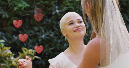 Image of hearts floating over diverse female married couple dancing. Pride, lifestyle and celebration concept digitally generated image.の写真素材