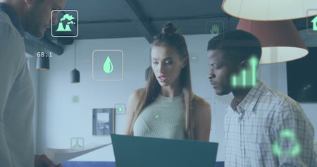 Image of ecology icons over diverse colleagues using laptop and discussing work in office. Global...