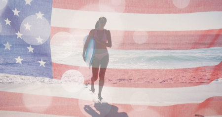 Image of light spots and american flag over caucasian woman carrying surfboard on sunny beach. America, summer, vacations, healthy lifestyle, patriotism and celebration, digitally generated image.の写真素材