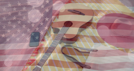 Image of american flag and light spots over guitar, smartphone and bag on beach towels in sun. America, summer, vacations, lifestyle, communication and patriotism, digitally generated image.の写真素材