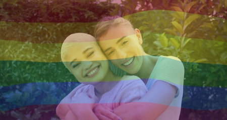 Image of rainbow flag over diverse female couple embracing. Pride, lifestyle and celebration concept digitally generated image.の写真素材