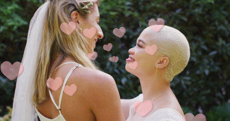 Image of hearts floating over diverse female married couple dancing. Pride, lifestyle and celebration concept digitally generated image.の写真素材