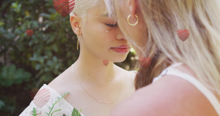 Image of hearts falling over diverse female couple embracing. Pride, lifestyle and celebration concept digitally generated image.の写真素材
