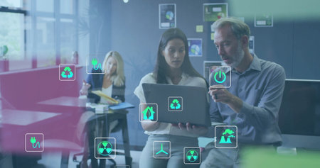 Image of ecology icons over diverse colleagues using laptop and discussing work in office. Global...