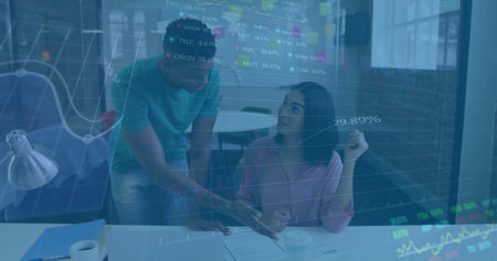 Financial data charts image over diverse colleagues discussing work in officeの写真素材