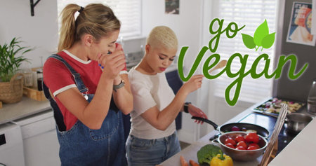 Image of go vegan text over gay lesbian couple dancing and cooking together at homeの写真素材