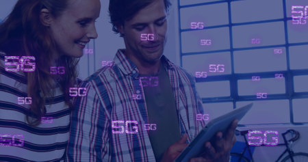 Image of 5g icons over happy caucasian male and female colleague using tablet at casual officeの写真素材