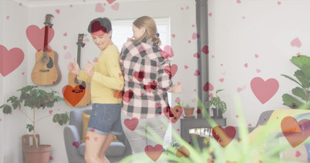 Image of heart emojis over happy caucasian female couple in love. Love, romance and celebration concept digitally generated image.の写真素材