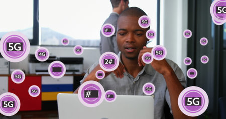 Image of 5g text and symbols in circles, african american man tired after working on laptop. Digital composite, multiple exposure, business, telecommunication, signs and technology concept.の写真素材