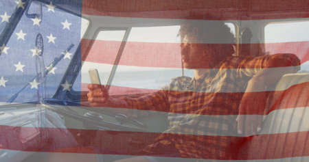 Image of American flag waving over biracial man on beach by seaside on summer holiday road trip in the background. American society diversity concept digital compositionの写真素材