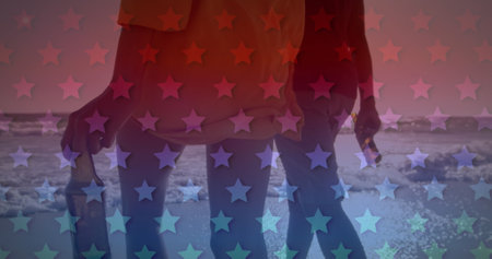 Image of American flag waving over biracial couple by seaside on summer holiday walking and holding beer bottles in the background. American society diversity concept digital composition.の写真素材