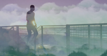 Image of clouds over african american man running at beach. health and fitness concept digitally...