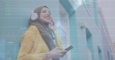 Image of financial data and graphs over biracial woman wearing headphones using smartphone. finance,...