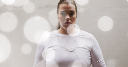 Image of spots of light over plus size caucasian woman in sports clothes flexing muscles. Sports, active lifestyle, urban living and happiness concept digitally generated image.の写真素材