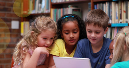 In school, diverse group of young students focusing on tablet. Caucasian and African American girls with blonde and black hair wearing colorful topsの写真素材