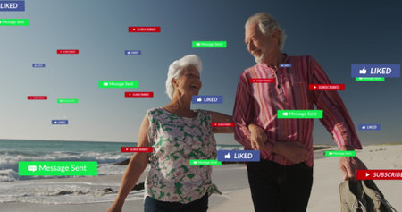 Image of social media text and icons over senior caucasian couple on beach. Global social media, digital interface, computing and data processing concept digitally generated image.の写真素材