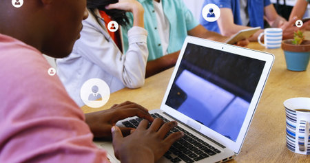 Image of multiple profile icons over diverse coworkers discussing and working on laptop. Digital...
