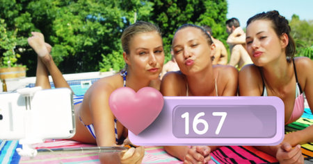 Close up of three Caucasian women laying on the beach tacking selfies. Digital image of a heart icon...