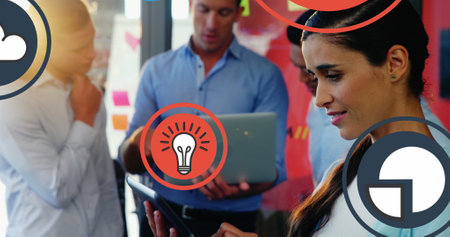 Image of multiple icons over biracial woman standing and using digital tablet in office. Digital composite, multiple exposure, business, ideas, globalization, cloud computing and technology.の写真素材