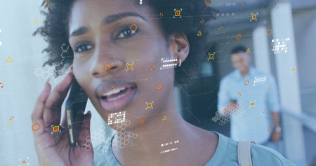 Image of data processing over african american woman with takeaway coffee talking on smartphone. Data, networks, digital interface, convenience and communication, digitally generated image.の写真素材